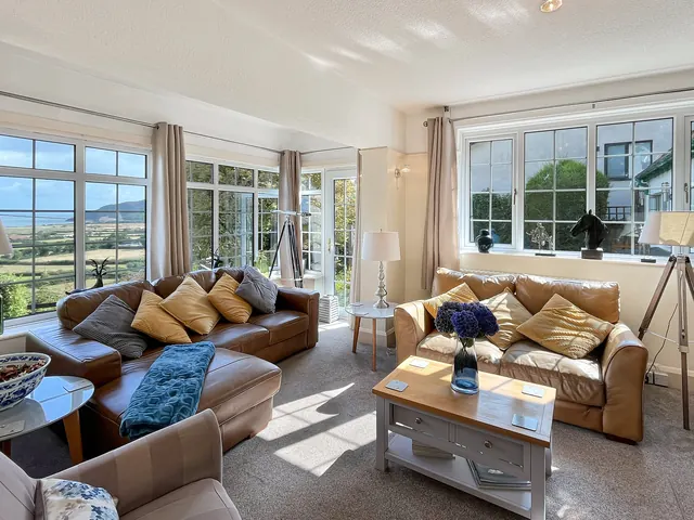 A sitting room with two leather sofas and tall windows on two sides, the bay in the distance