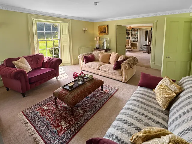 A drawing room with pale green walls, plum velvet sofas and a tall sash window onto the moor