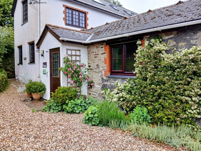 A whitewashed cottage under a slate roof, roses climbing the porch, gravel to the door