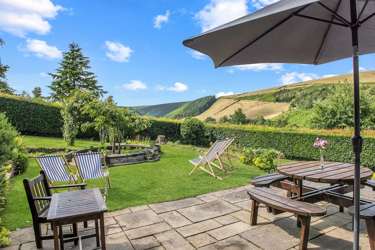 The terrace at Oare Manor Cottage, with a table and chairs looking across the garden to the wooded hills