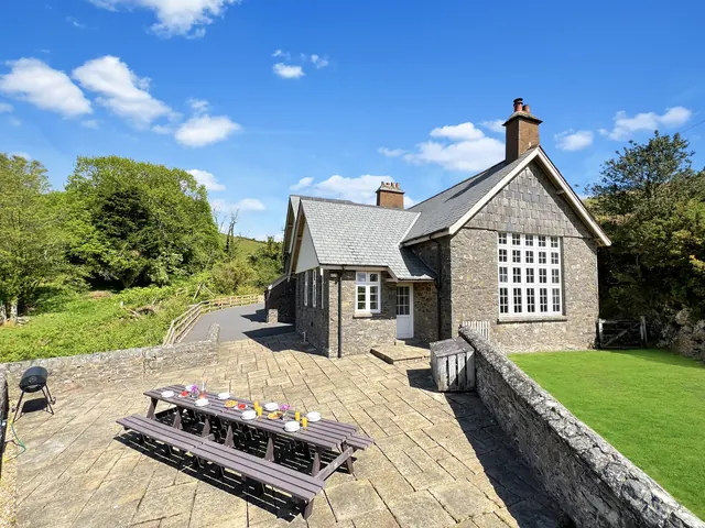 The old school from the lawn: stone gables, tall windows, a long picnic table on the terrace